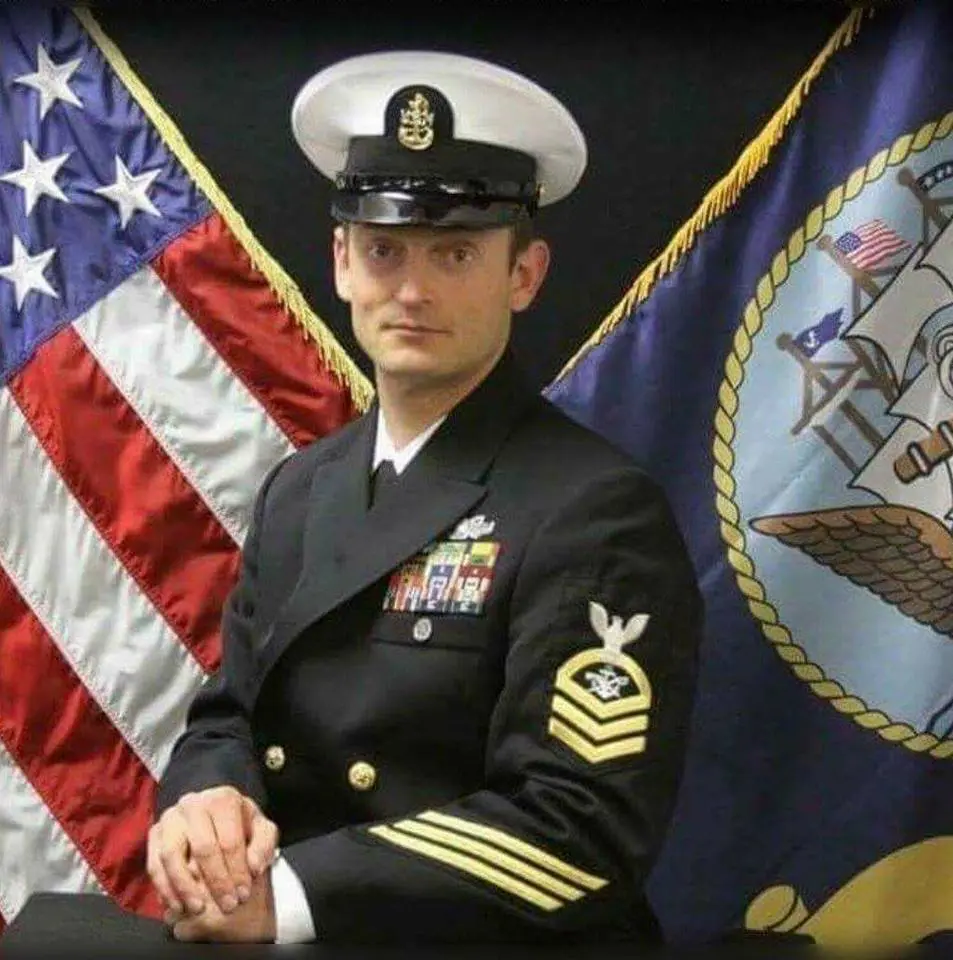 Image of SBC Zacharias E. Buob in his formal blue Navy uniform with his military decorations on his uniform left side of front uniform coat. Behind Zach are to the left the American flag. To his right is the Navy flag.