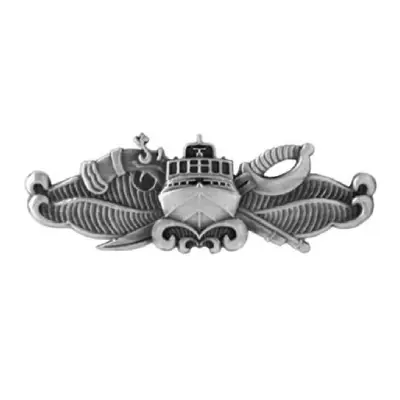 Image of silver Special Warfare Combatant Crew Member Pin. The pin is designed with front of a boat with a six window windshields, has antennas, radar dome with waves curling up below boat as well as on both sides of the boa. Sticking out from the top left of boat is a flint lock gun handle. To the right side of boat sticks out a ceremonial sword handle.