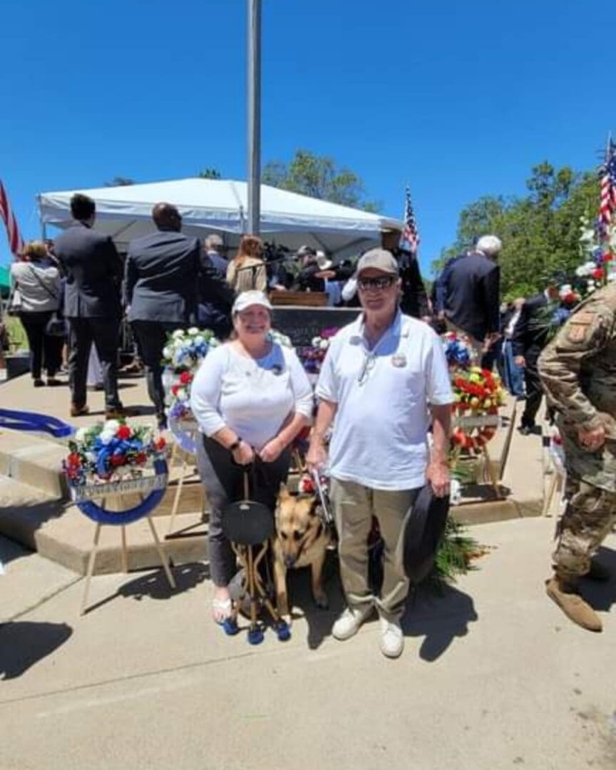 Photo of Gold Star Parents of SBC Zach Buob, Kathy & Gary are at Memorial Day event at Oak Hill Memorial Park standing with service dog, Sammy, between them.