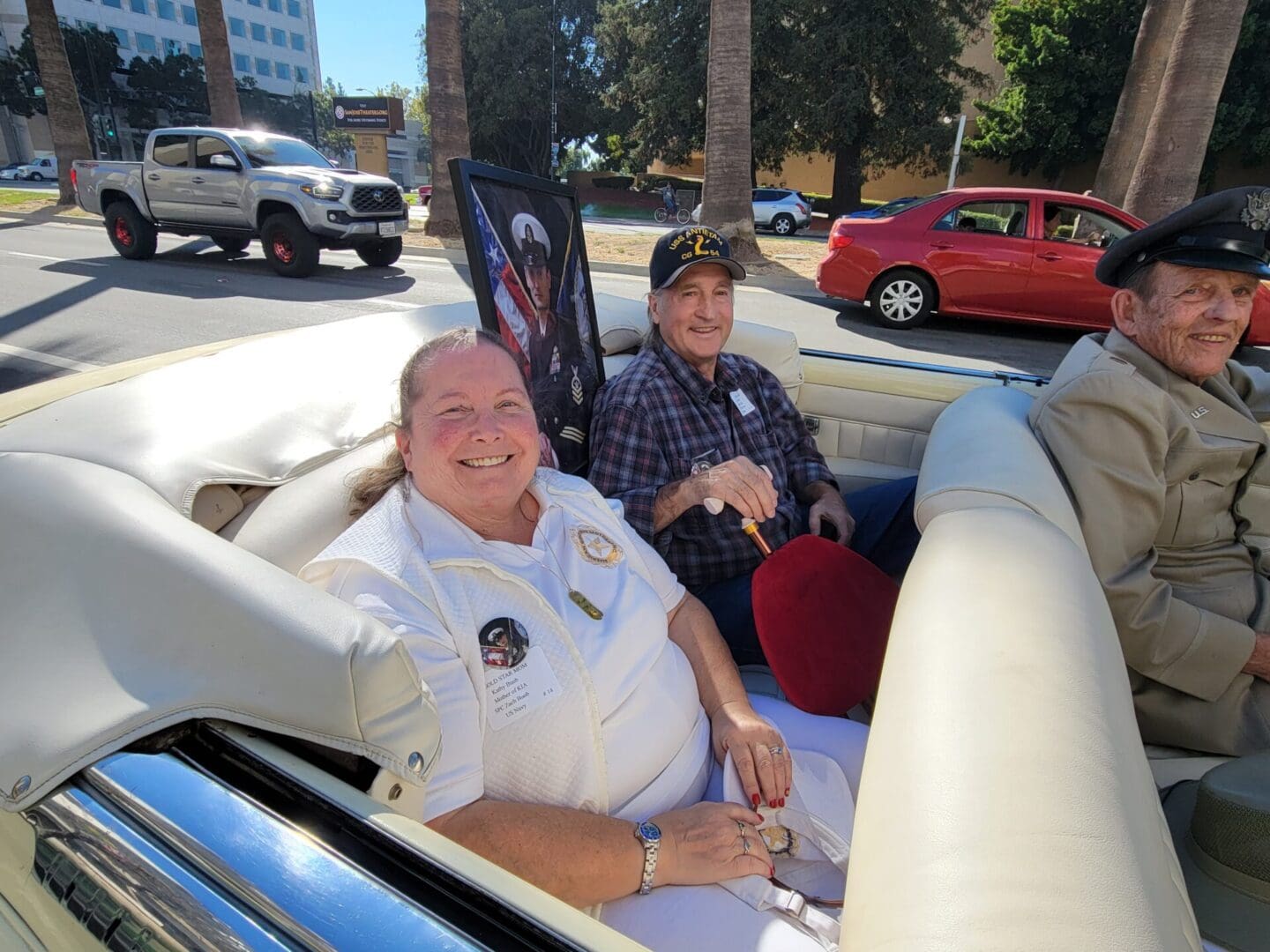 Photo of SBC Zach Buob's Gold Star Parents-Kathy & Gary at San Jose Veteran Day Parade sitting in convertible car with photo of Zach in Navy blue uniform between them.