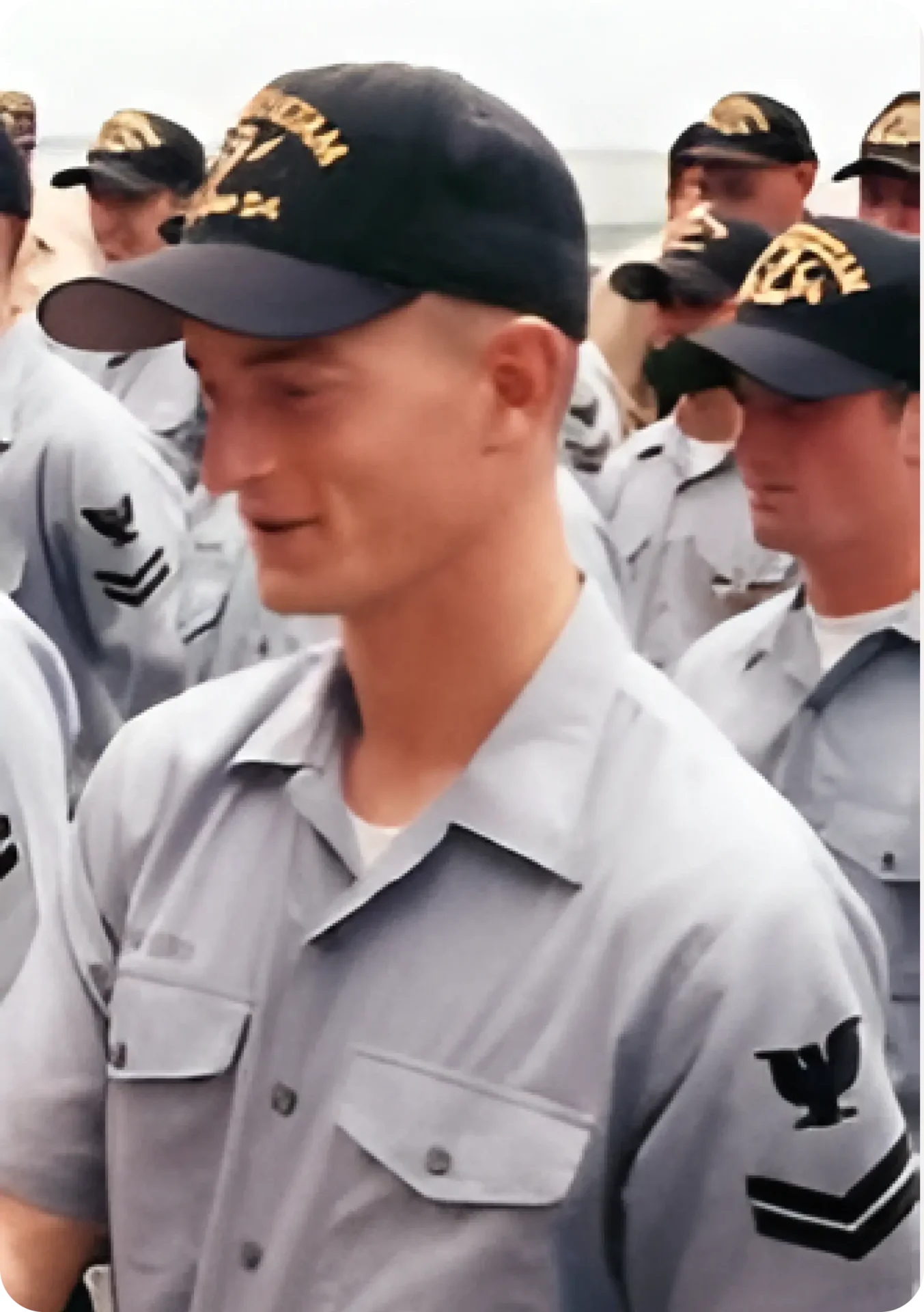 Image of sailor E-2 Zach Buob receiving an award while a Gunner's Mate on the USS Antietam. Zach is wearing a dark blue ball cap withUSS Antietam name on it. He wears a light blue Navy work shirt with and eagle patch and two strips below it. There are a group of sailors in rows around him standing at attention.